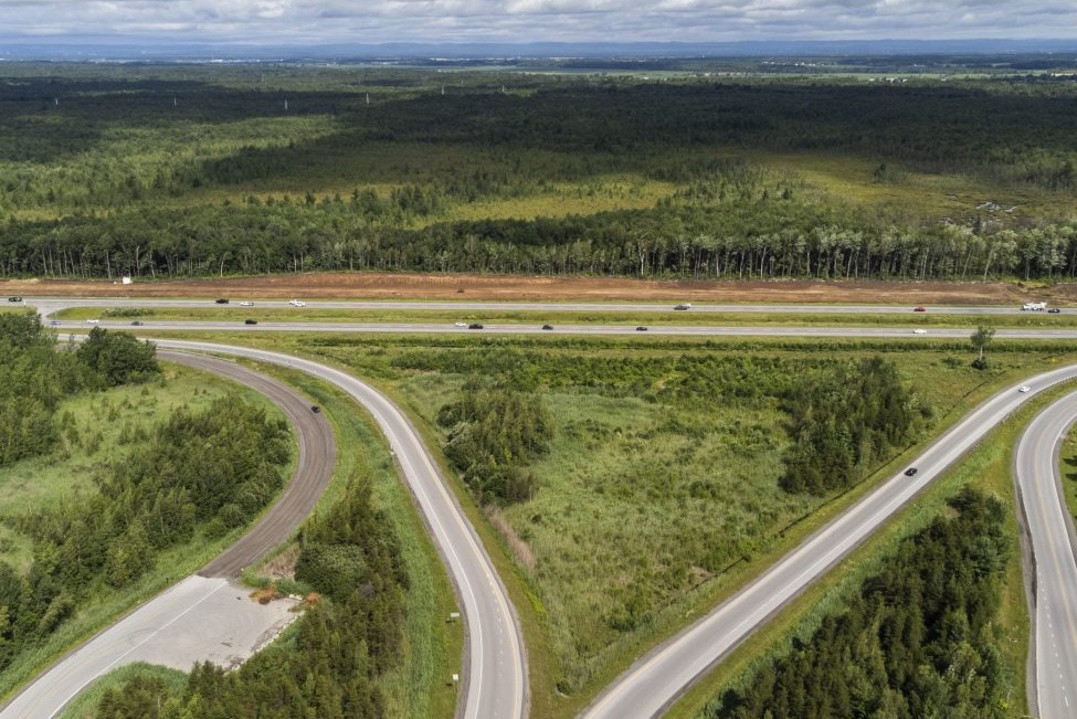 Vue aérienne d’un échangeur autoroutier entouré de vastes forêts de conifères et de feuillus sous un ciel nuageux