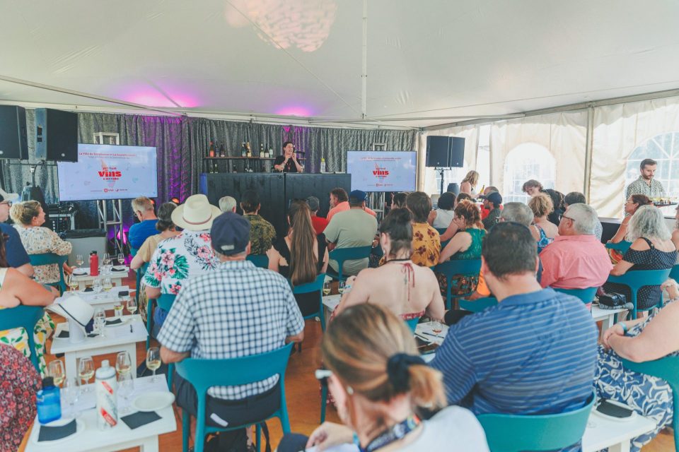 Conférence sur le vin sous une tente lumineuse, public attablé avec des verres devant deux écrans