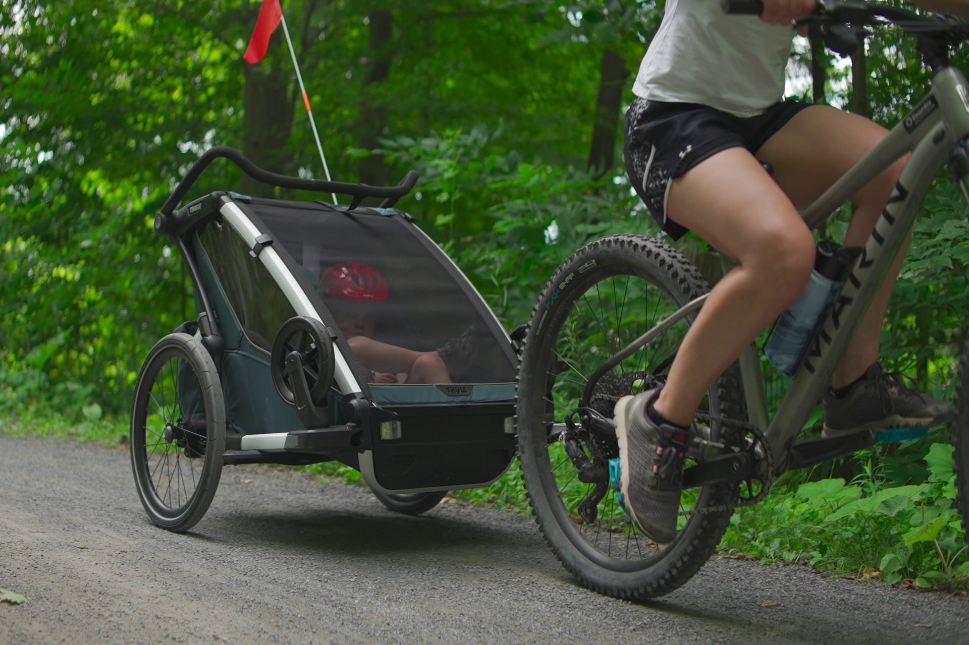 Cycliste pédalant sur un sentier forestier en remorquant une remorque vélo Thule avec un enfant casqué à l’intérieur