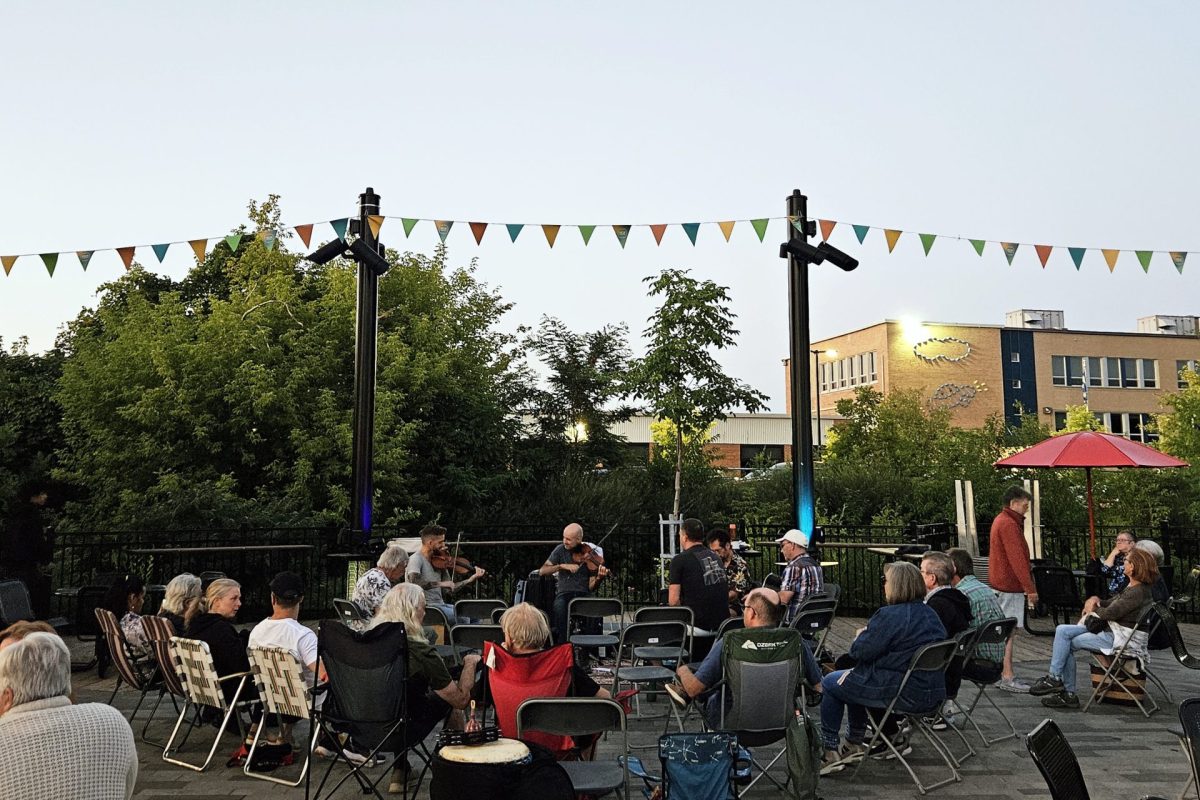 Concert en plein air au crépuscule, des musiciens jouent du violon devant un public assis sur une place ornée de fanions