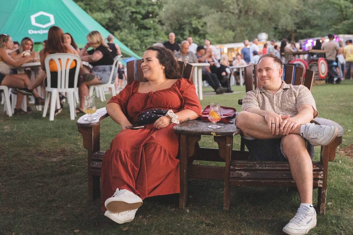 Deux personnes assises à une table en bois lors d'un festival en plein air, des verres posés devant elles