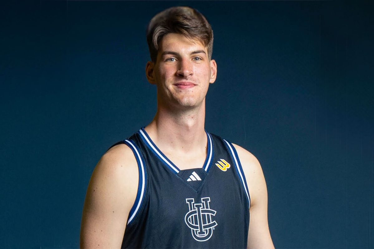 Portrait officiel d’un joueur de basketball de l’UC Irvine posant en maillot bleu marine sur fond bleu foncé